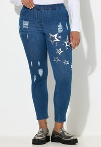 Wąskie dżinsy z ciemnoniebieskiego denimu z przetarciami i srebrnymi wzorami gwiazdek. Elastyczny pas z kieszeniami; ogólnie smukły i dopasowany krój.