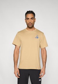 Μπεζ βαμβακερό μπλουζάκι με στρογγυλή λαιμόκοψη και κοντά μανίκια. Διαθέτει μπλε λογότυπο στο επάνω αριστερό μέρος. Ομαλή υφή.