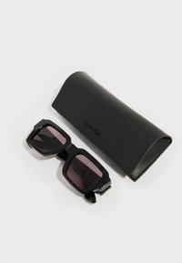 Czarne okulary przeciwsłoneczne Calvin Klein z prostokątnymi oprawkami, ciemnymi soczewkami i detalem zawiasu, wraz z czarnym etui ochronnym.