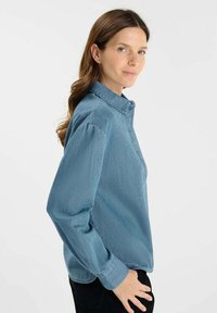 Lichtblauwe denimoverhemd met een kraag, knoopsluiting en lange mouwen. De stof heeft een licht gestructureerde afwerking. Eenvoudig ontwerp, geen patronen.