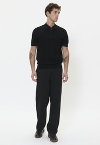 Black knit polo shirt with a zipper, short sleeves, and ribbed cuffs, paired with wide black trousers and dark shoes. Minimalist design.