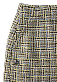 Gros plan sur un tissu tweed multicolore texturé avec des fils jaunes, bleus, bruns et blancs, et une petite étiquette métallique ronde près d'une poche cousue.