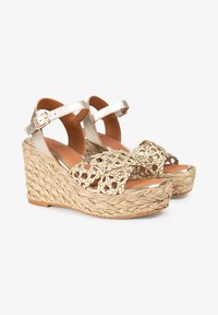 Sandales à plateforme tissées en or avec une semelle en jute tressé, dotées d'une sangle métallique et d'un détail en crochet décoratif sur le dessus.