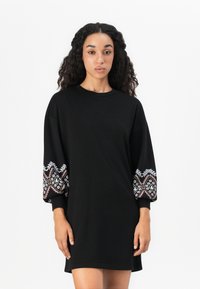 Zwarte oversized jurk met lange, versierde mouwen met kleurrijke geometrische borduursels en een ontspannen pasvorm. Gladde stoftextuur.