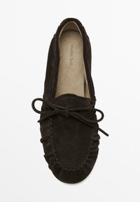 Hnědá semišová mokasínová bota s měkkou texturou, kulatou špičkou, dekorativním prošitím a mašlí na přední straně. Viditelná vnitřní podšívka.