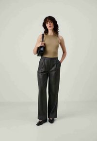 Beige mouwloos topje, hoge taille zwarte pinstripe broek, strakke zwarte handtas, puntige zwarte schoenen, gladde textuur, op maat gemaakte pasvorm.