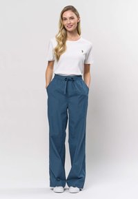 Lagana tamnoplava hlače s elastičnim pojasom i vezicom, bočnim džepovima i ležernim krojem, uparene s bijelom rebrastom majicom kratkih rukava.