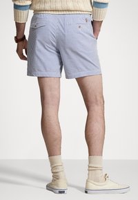 Miestne modro-biele pruhované šortky s zadnými vreckami, kombinované so smotanovými ponožkami po členky a svetlými teniskami. Pevná látka, neformálny dizajn.