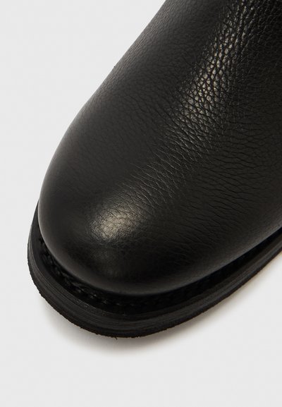 Fekete bőr cipő texturált felülettel, lekerekített orral és varrott fekete talppal. A felső anyag sima, finom fényű.