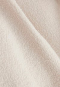 Šviesiai rožinė veliūrinė medžiaga su minkšta, tekstūruota paviršiaus struktūra, išsiskirianti lygia danga ir smulkia, tolygia struktūra.