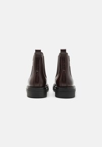 Botas Chelsea de cuero marrón con paneles laterales elásticos y tiradores, con una suela de goma negra duradera y textura suave.
