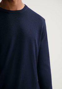 Maglione in lana blu navy a maniche lunghe con scollo rotondo e texture liscia, con dettagli sulle cuciture delle spalle e sui polsini.