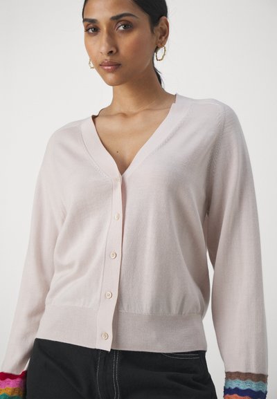 Cardigan rose clair avec un col en V, une fermeture par boutons et de longues manches. Les poignets présentent des accents colorés en forme de scallop. Texture douce, silhouette ajustée.