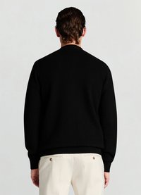 Pull noir en maille avec un col rond, des poignets côtelés et un motif texturé. Vue de dos, associé à un pantalon clair.