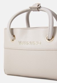 Beige textúrájú bőrtáska aranyszínű kiegészítőkkel, dupla rövid fogantyúkkal és a "VALENTINO" felirattal a fronton.
