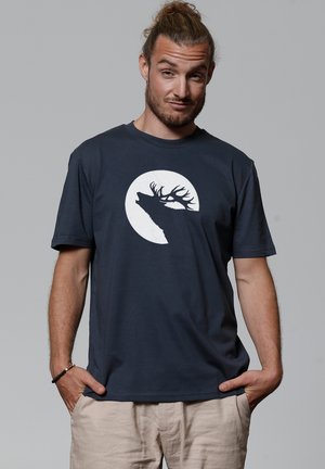 Navyblauwe katoenen T-shirt met een witte silhouette van een hert tegen een cirkelvormig maandesign. Korte mouwen en een relaxte pasvorm.