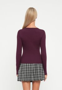 Fitted long-sleeve top in deep purple ribbed fabric paired with a flared black and white plaid skirt, featuring a smooth hem and simple neckline.