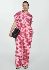 Woman wearing matching pink, red, and white wavy striped shirt and pants, holding a black textured clutch and wearing black sandals.