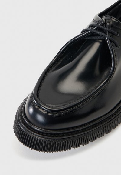 Μαύρο γυαλιστερό δερμάτινο παπούτσι με παχύ αυλακωτό πέλμα και μαύρα κορδόνια, εμφανιζόμενο σε κοντινή γωνιακή λήψη.