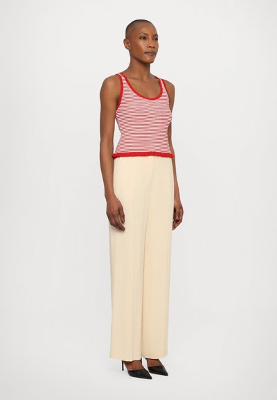 Débardeur rayé rouge et blanc avec un ourlet volanté, associé à un pantalon large crème et des escarpins noirs à talons pointus. Tissu lisse, design ajusté.