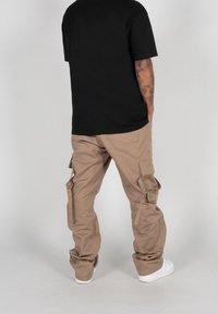 Pantaloni cargo beige con più tasche laterali, vestibilità ampia e una texture leggermente stropicciata, abbinati a una t-shirt nera e sneakers bianche.