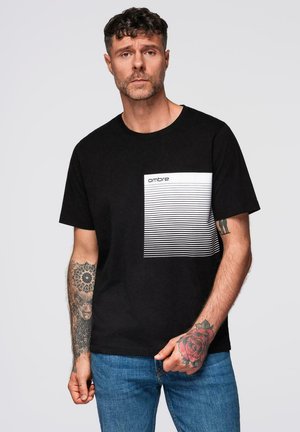 T-shirt noir à manches courtes avec un design de poche blanche rayée horizontale portant le mot "ombre" dans une police moderne. Matériau en coton.