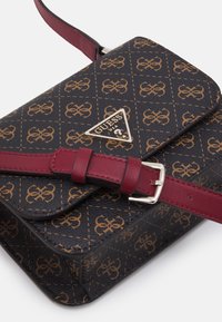 Bolso sintético negro con logo y estampado dorado. Cuenta con una correa burdeos y un cierre de plata. Diseño estructurado con cierre de solapa.