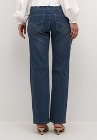 Jeans in denim blu a gamba larga con tasche posteriori, dettagli di cucitura discreti e orlo alla caviglia. Indossati con scarpe con tacco beige.
