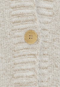 Krämfärgad strukturerad tyg med ett randigt mönster och en guldfärgad knapp med två hål, som framhäver den mjuka, fluffiga texturen.