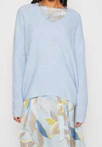 Jasnoniebieski sweter dzianinowy z dekoltem w kształcie litery V, luźny krój i długie rękawy. Nosić na kwiatowej sukience w jasnoniebieskim i kremowym kolorze.