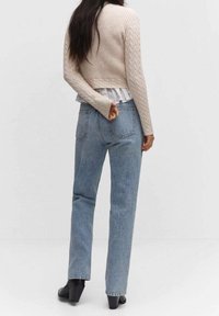 Pull court beige en maille côtelée porté sur une chemise blanche à volants, associé à un jean droit bleu clair. Bottines noires à talons complètent la tenue.