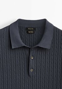 Navy blue knitted polo shirt with a textured cable pattern, featuring a flat collar and two-button placket. Soft cotton material.