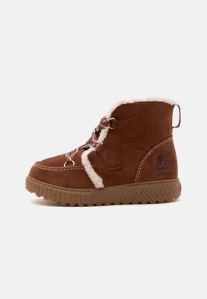 Bottine imperméable en daim marron avec doublure en polaire blanche, lacets à motifs, semelle robuste et logo Sorel sur le côté.