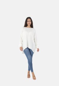 Witte, oversized gebreide trui met een ronde hals en drop schouders, gecombineerd met skinny blauwe jeans en doorzichtige haksandalen.