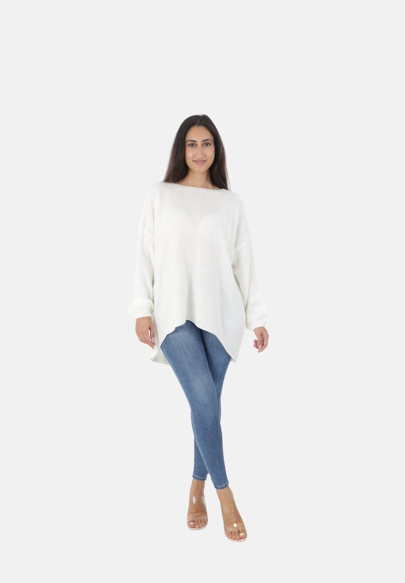 Witte, oversized gebreide trui met een ronde hals en drop schouders, gecombineerd met skinny blauwe jeans en doorzichtige haksandalen.