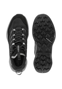 Schwarze Sportschuhe mit einem texturierten Obermaterial und grauen Akzenten, einem auffälligen Profilmuster auf der Gummisohle und einer Schlaufe an der Ferse.