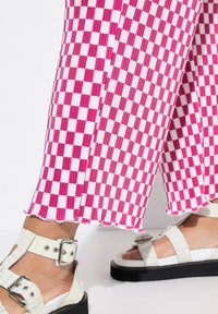 Pantaloni a quadri rosa e bianchi con texture a costine, caratterizzati da un orlo arricciato; abbinati a sandali bianchi con suola platform nera.