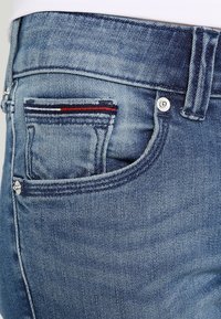 Vaqueros de mezclilla azul claro con un corte clásico, que cuentan con un pequeño bolsillo con detalles de rayas rojas y azules y acentos de hardware plateado.