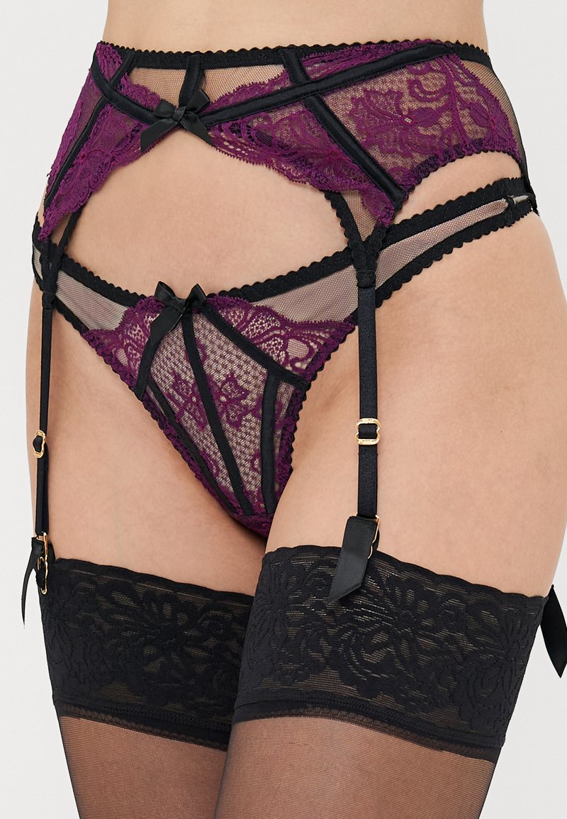 Garter belt en dentelle noir et violet, avec des motifs floraux, des strap ajustables et de petits nœuds en satin. Comprend des bas transparents.