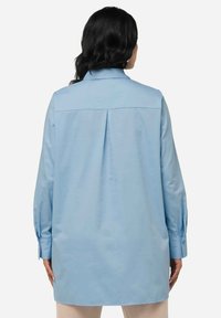 Camicia blu chiaro con piega posteriore, maniche lunghe e polsini con bottoni. Tessuto liscio e leggero con colletto e lunghezza estesa.