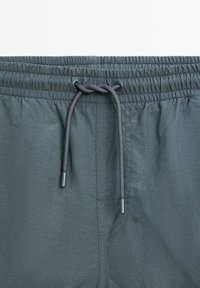 Shorts con cintura elasticizzata in tessuto grigio scuro, dotati di chiusura con cordoncino e tasca laterale. Texture liscia con dettagli di cucitura discreti.