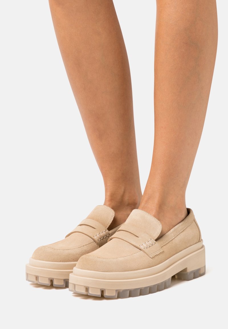 Mocassins à plate-forme en daim beige avec semelles épaisses en caoutchouc portés pieds nus, vue de face sur un fond clair.