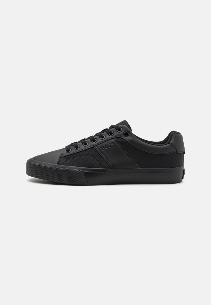 Black sneakers with a mix of smooth and textured materials, featuring a low-top design, round laces, and a patterned side panel.