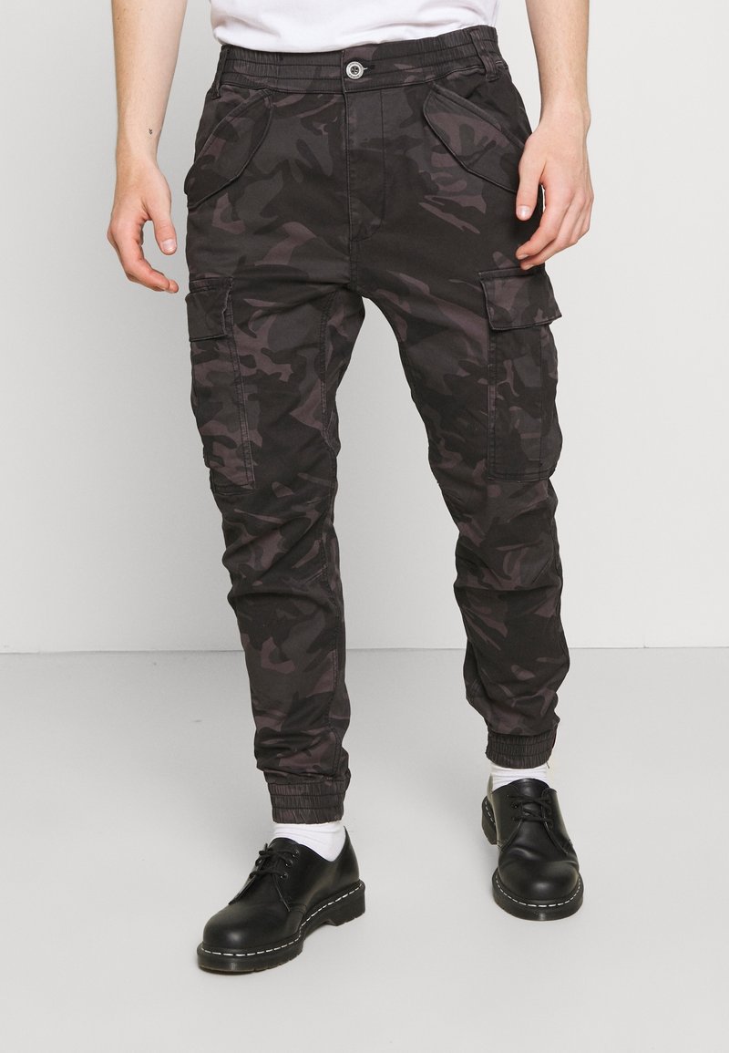 Mustat ja harmaat puuvillaiset maastokuvioiset cargo-housut, joissa on joustava vyötärönauha, useita taskuja ja kapeat lahkeet joustavilla resoreilla.