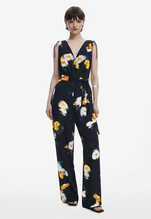 Floral jumpsuit with a deep V-neck, navy background, yellow and white flowers, adjustable tie straps, and a matching fabric belt at the waist.