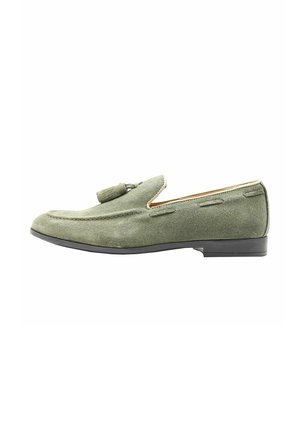 Mocassini in suede verde con suola in gomma nera bassa, dettaglio con nappina, cuciture e design classico.
