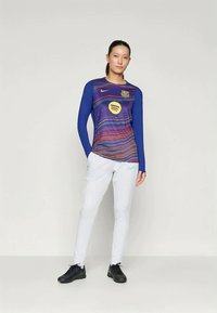 Garais piedurkņu zils un daudzkrāsains sporta krekls ar FC Barcelona logo un Spotify emblēmu, apvienots ar baltām biksēm un melnām kurpēm.