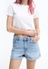 Camiseta de algodón blanca de manga corta con un detalle plateado en el cuello, combinada con pantalones cortos de mezclilla azul claro con puños enrollados y bolsillos frontales.