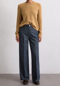 Mustard knit sweater with a textured finish and crew neckline, paired with dark high-waisted wide-leg denim jeans featuring a button closure.