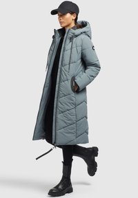 Dlhý, svetlomodrý puffový kabát s kapucňou, s diagonálnym prešitím, sťahovacími šnúrkami a bočnými vreckami. Nosený s čiernym oblečením a čižmami.